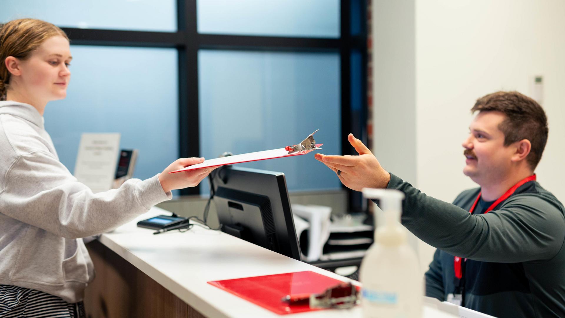 A medical provider smiles as he takes a clipboard from a person. 