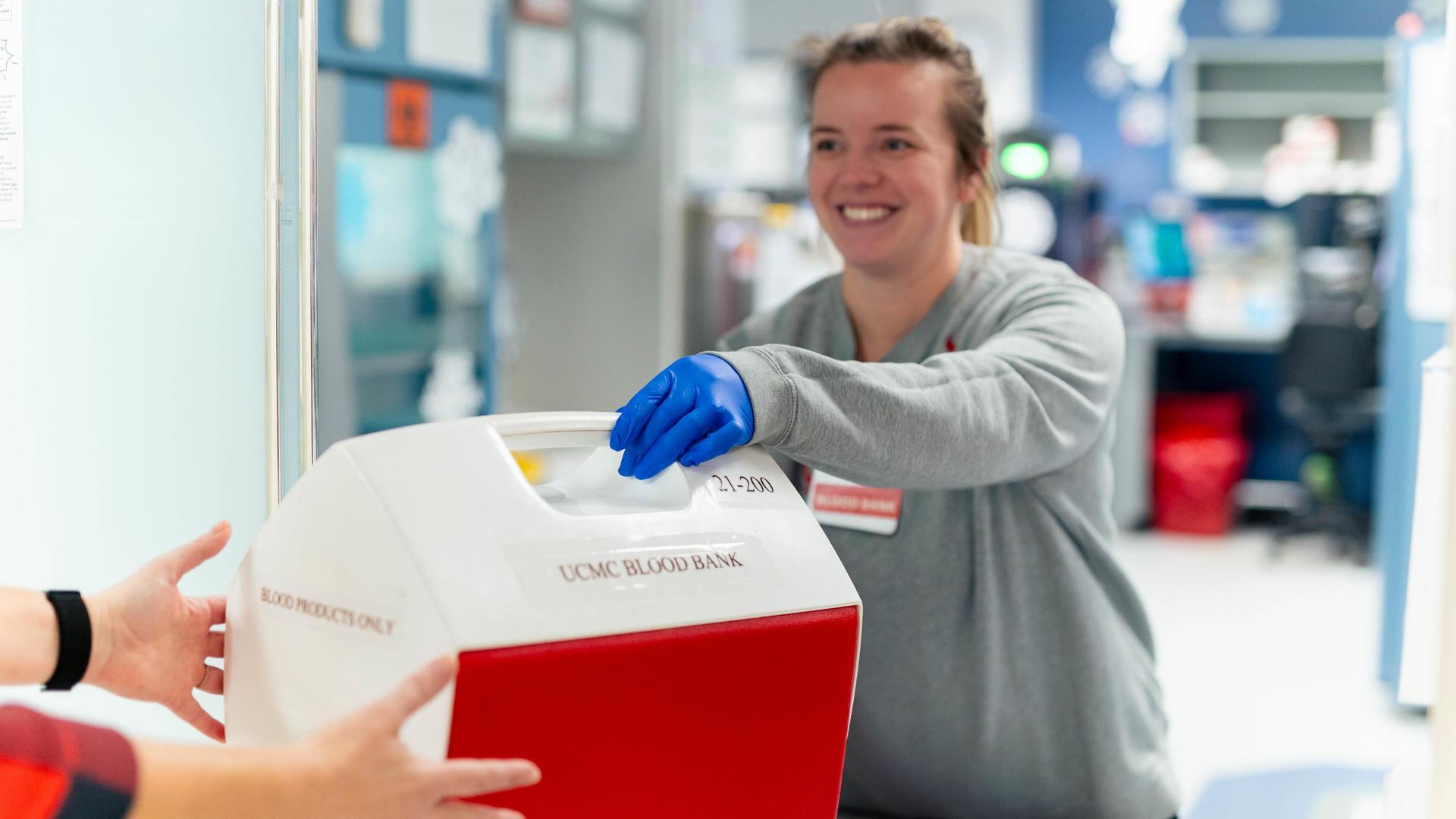 A medical provider in a lab hands a cooler to a person. 