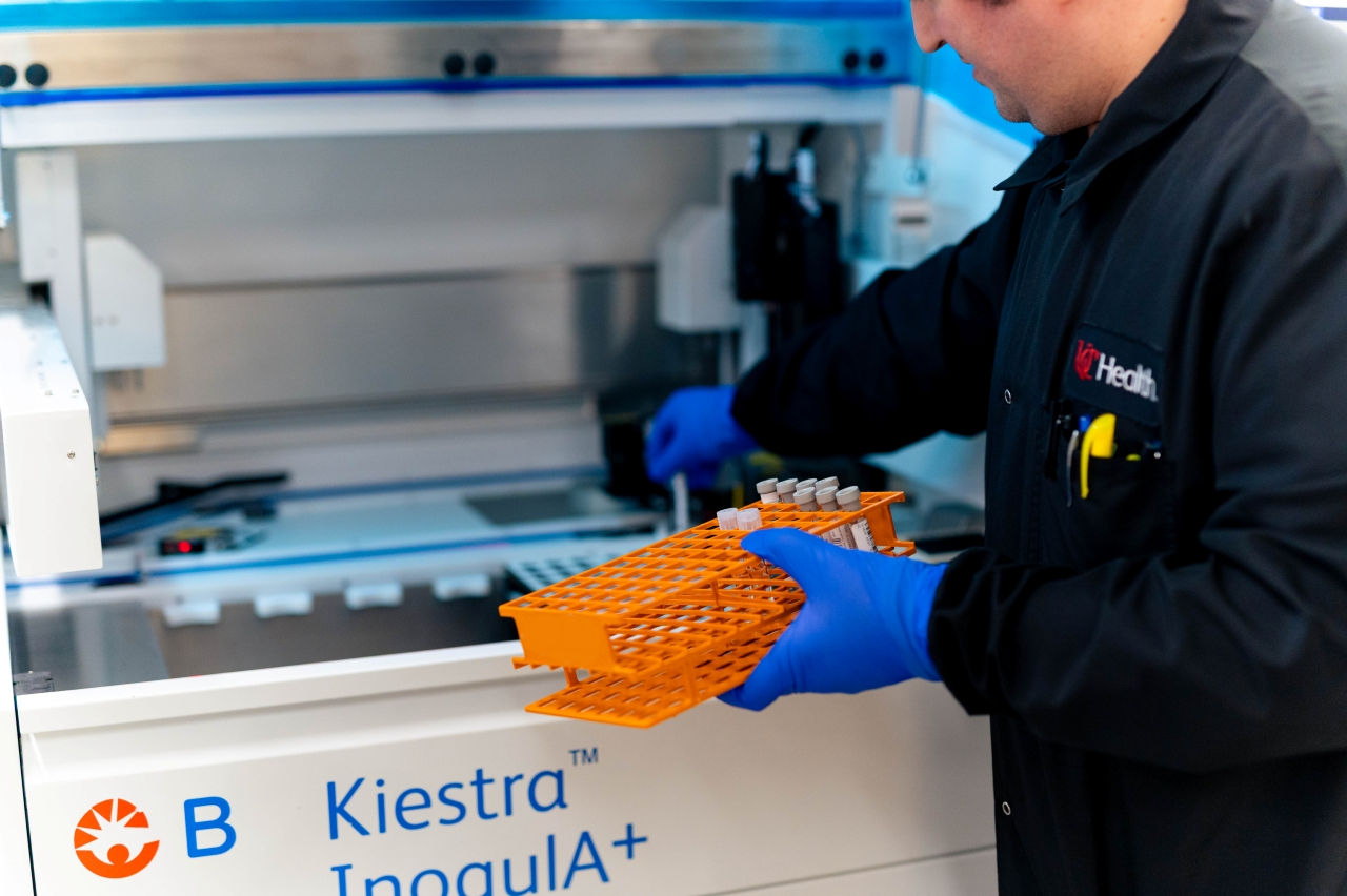 Tech works in a clinical lab with an orange container. 