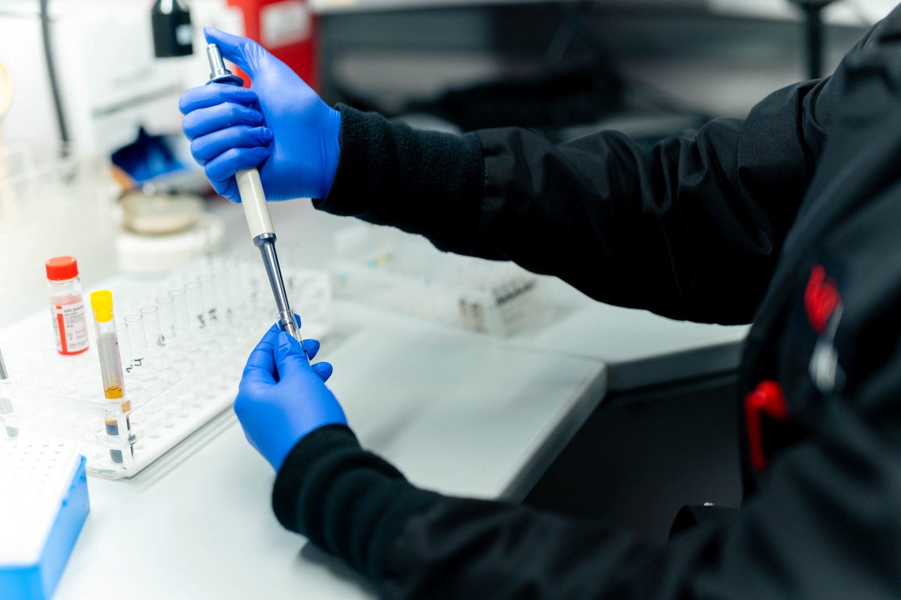 Lab specialist wearing blue gloves working with a vial. 