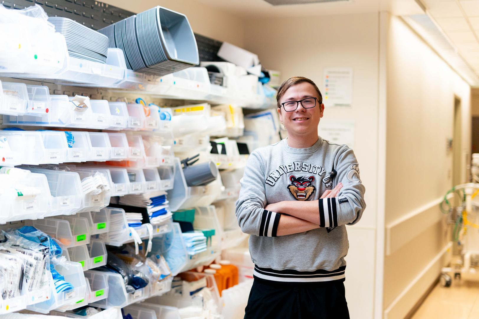 Young man poses in front of a prescription shelf at a pharmacy