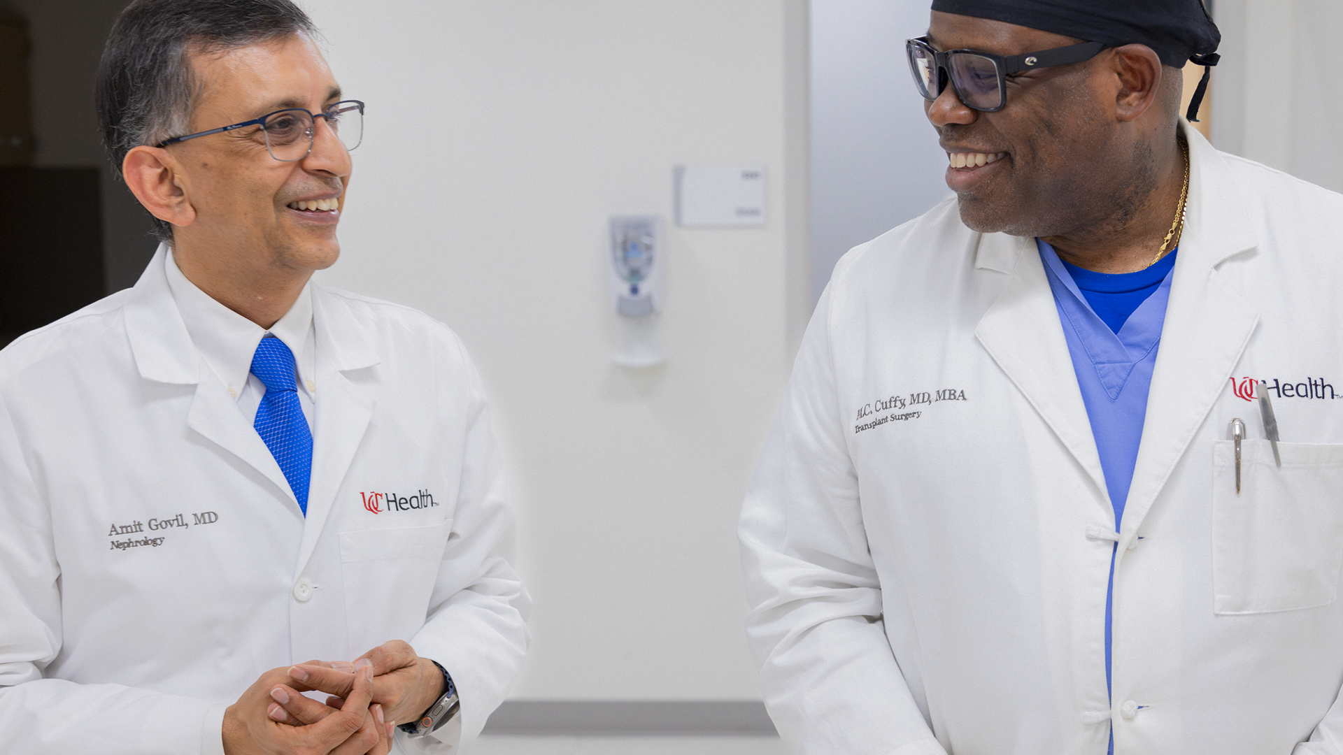 Two physicians talk as they walk through a hallway. 