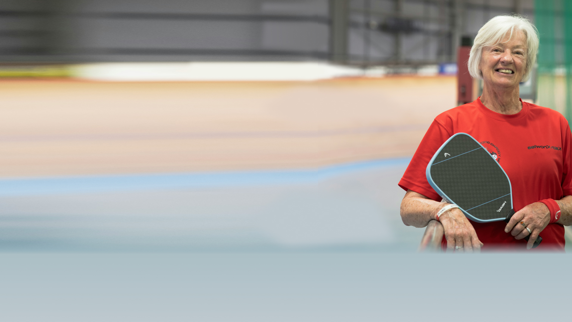 Smiling woman holds pickleball paddle at pickleball facility.