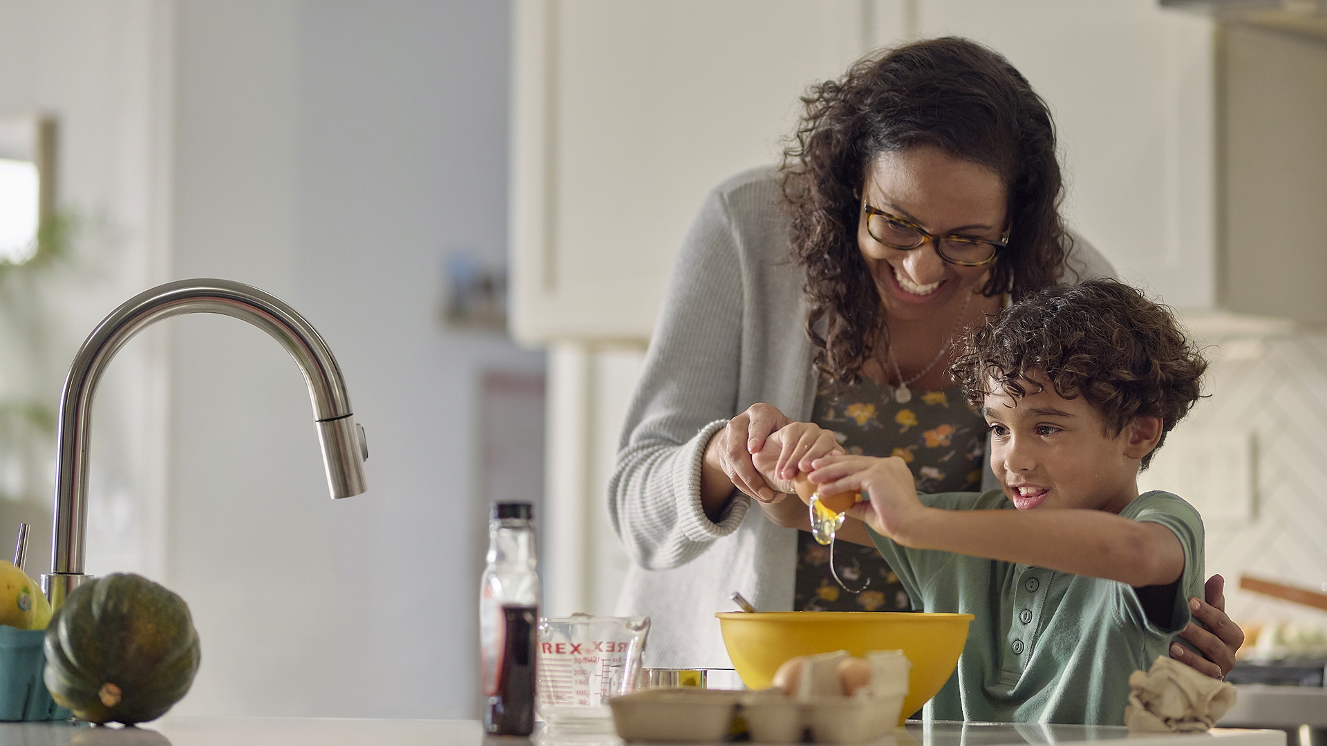 Mother and son smiling and breaking egg over kitchen sink.