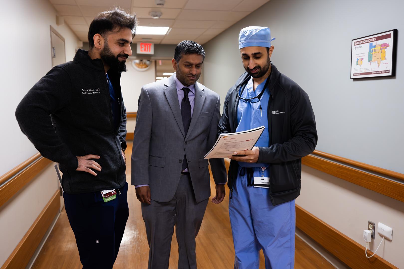 Three physicians meet and talk in a hallway. 