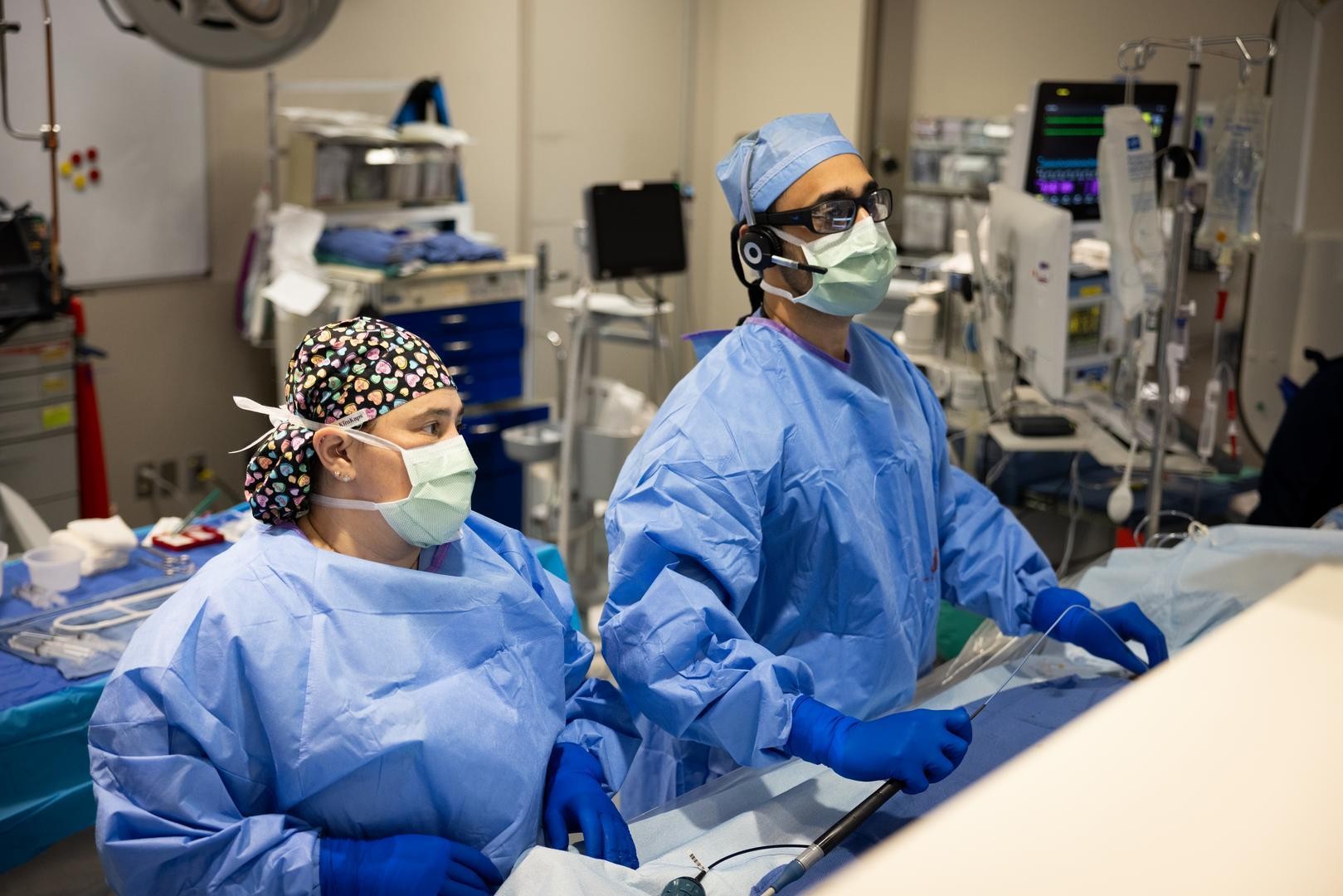 Physicians in masks and scrubs perform a medical procedure.