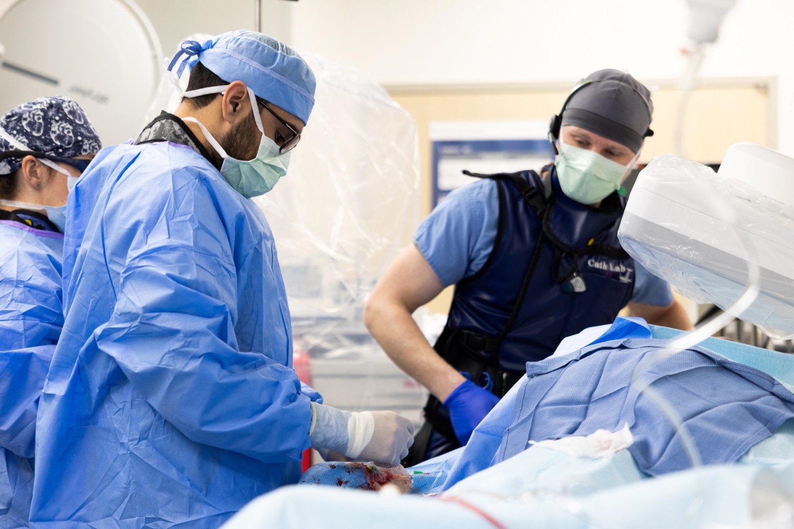 Medical providers in masks and scrubs perform a medical procedure.