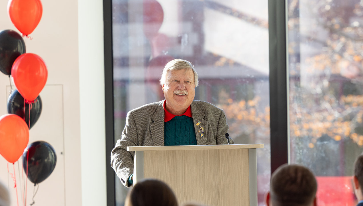 Dr. Bill Shula shares his story at a podium surrounded by black and orange balloons 