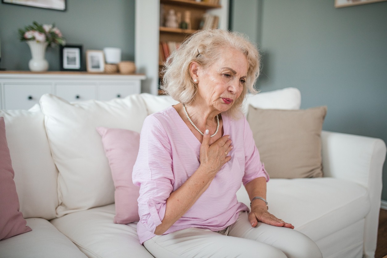 Woman sits on couch and feels her heart while breathing