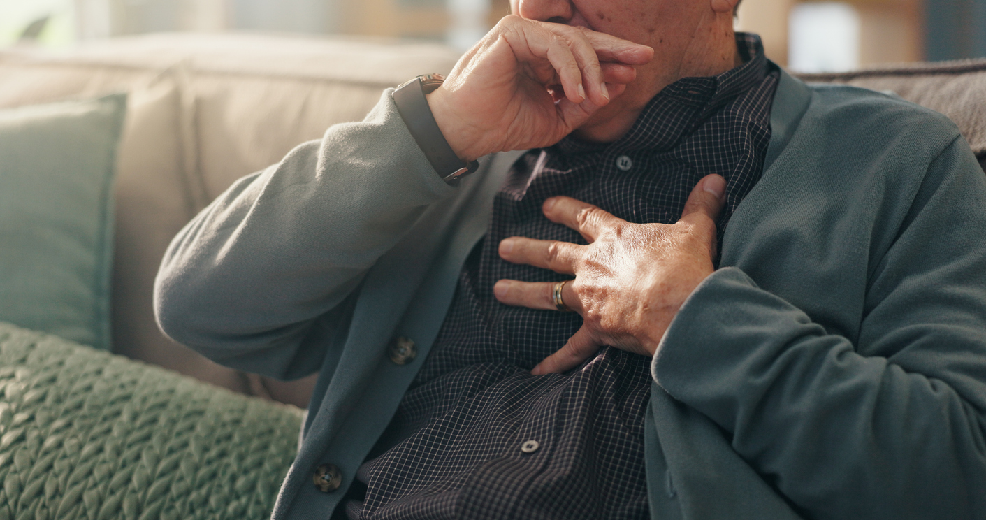 Man puts his hand over his chest while sitting on the couch