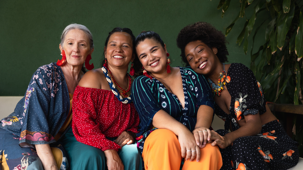 Four women sitting on a sofa and smiling at camera.