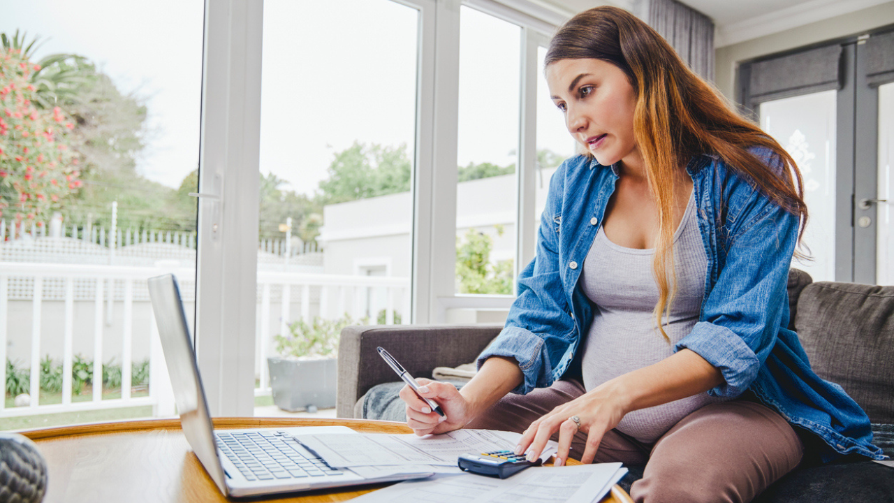 Woman who is pregnant works with a laptop and calculator from a couch