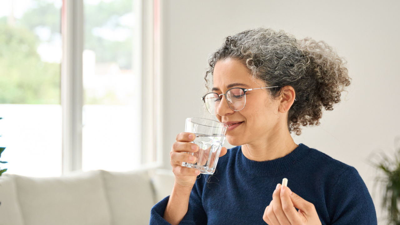 Woman in her 40s takes a vitamin with a drink of water