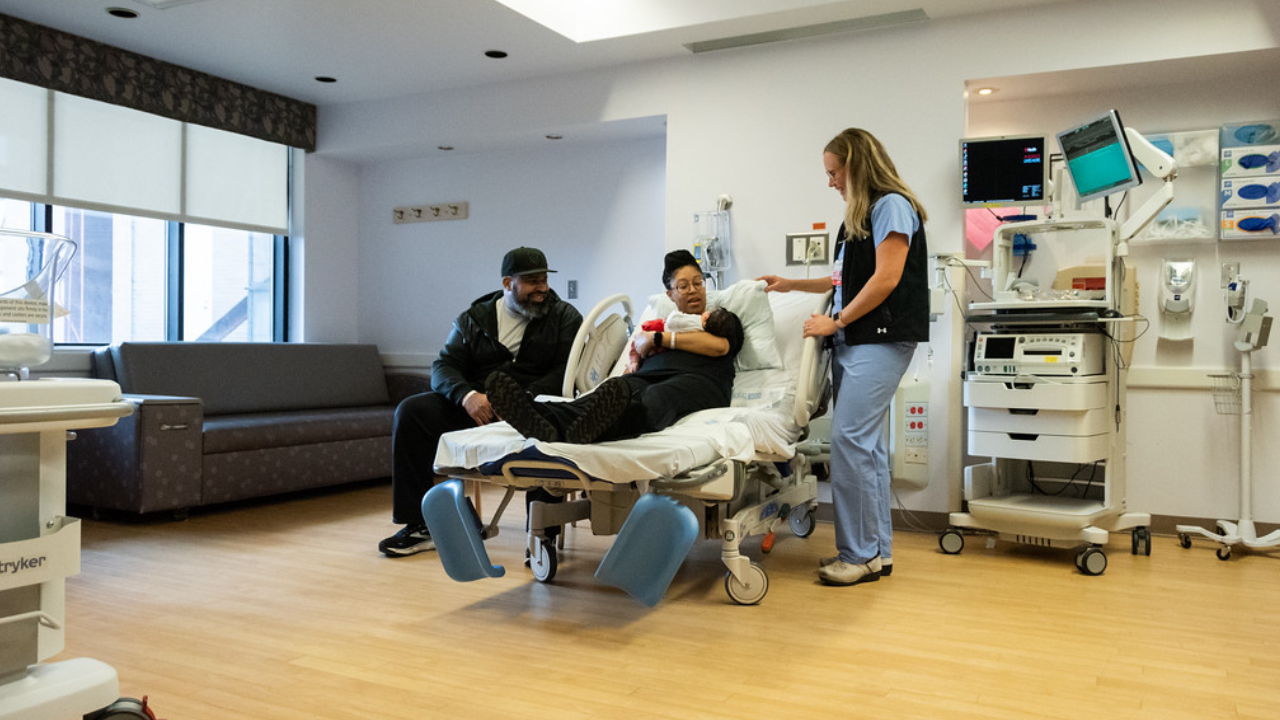 Family holds their new daughter while talking with a healthcare provider at UC Health in Cincinnati.
