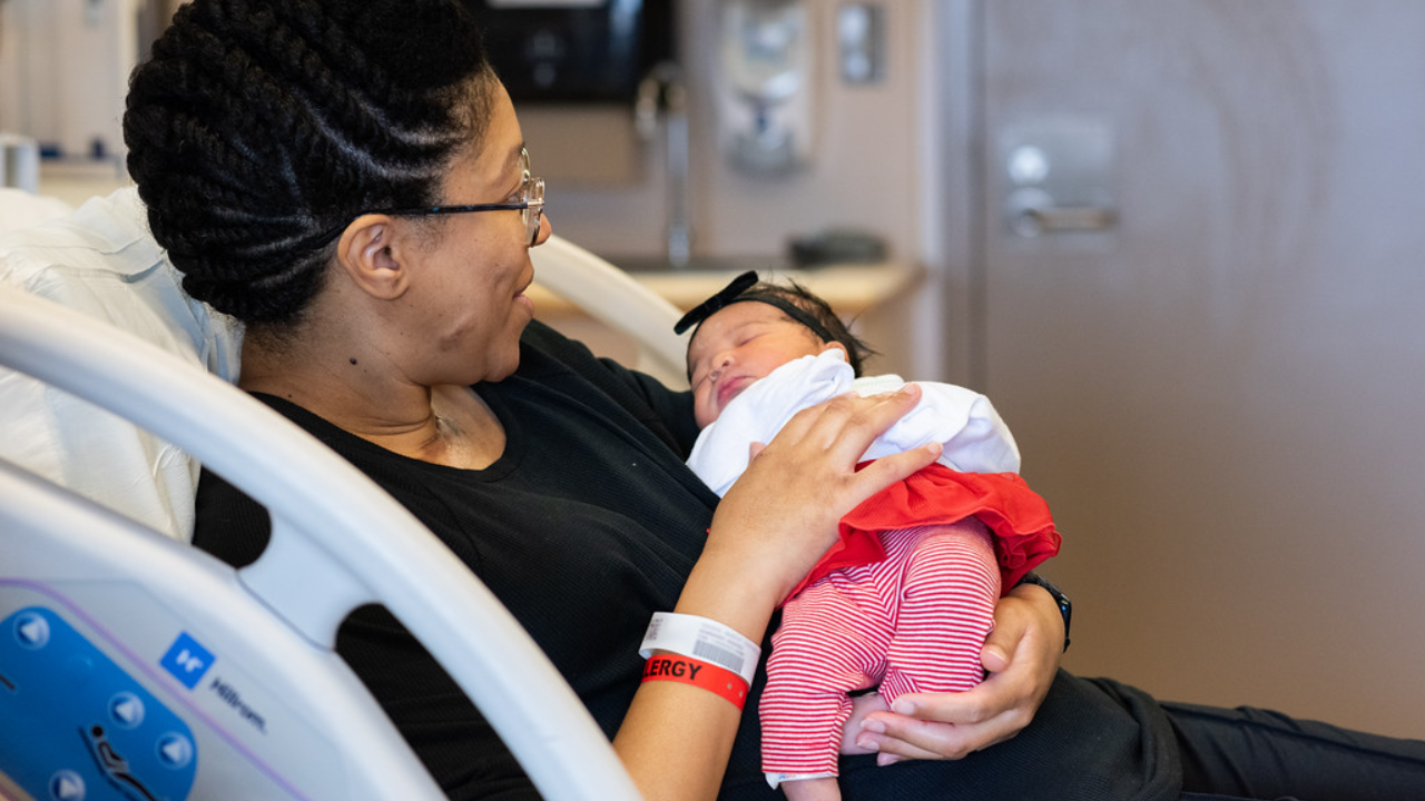 Black woman smiles while holding her new baby at UC Health in Cincinnati