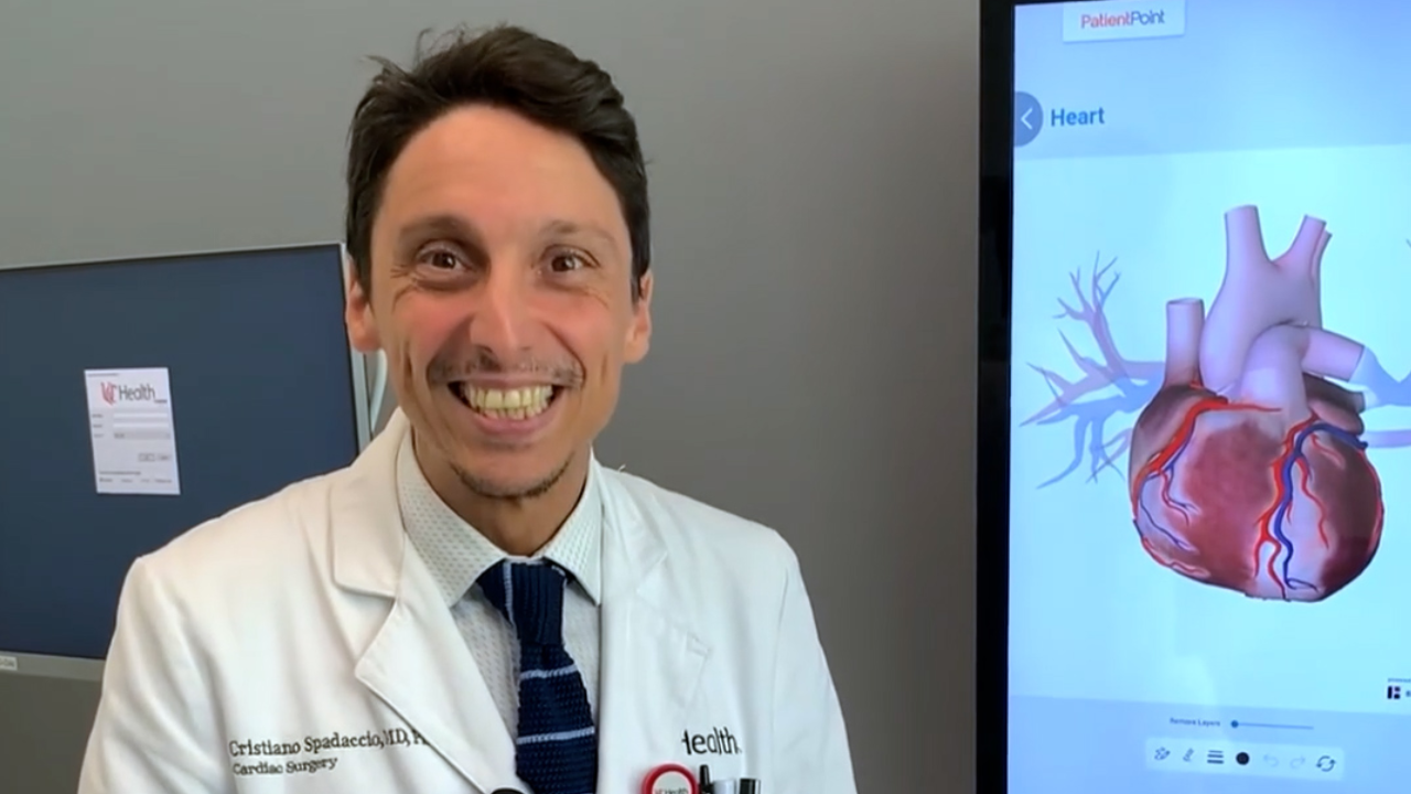 Dr. Spadaccio smiles next to a screen showing a heart diagram