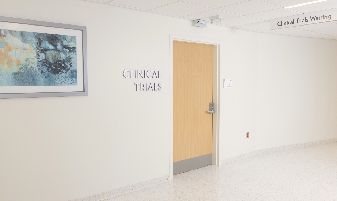 Hallway with an art print and a sign next to a door that says Clinical Trials. 