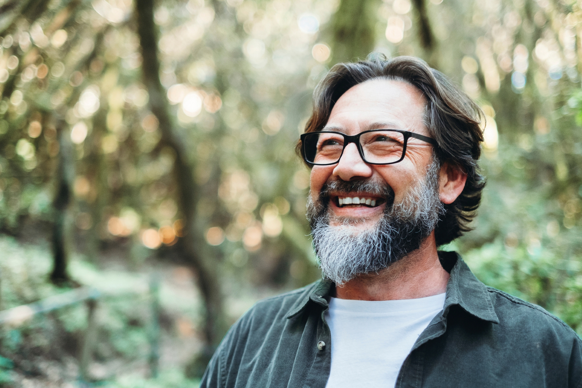 Man smiles as he hikes in a wooded area. 