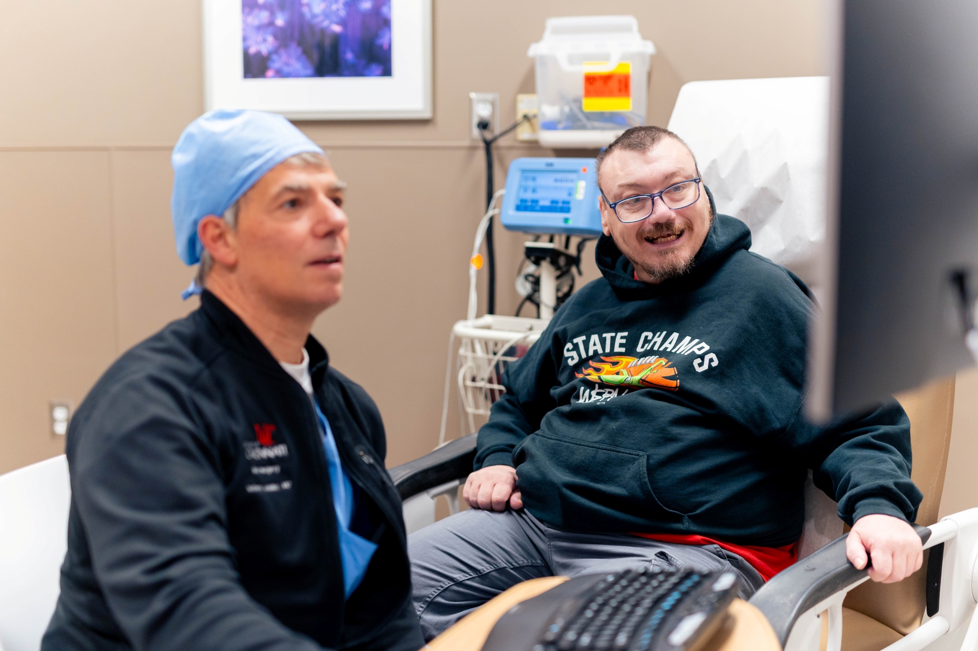 Physician types something into a computer while a patient looks at the screen and smiles. 