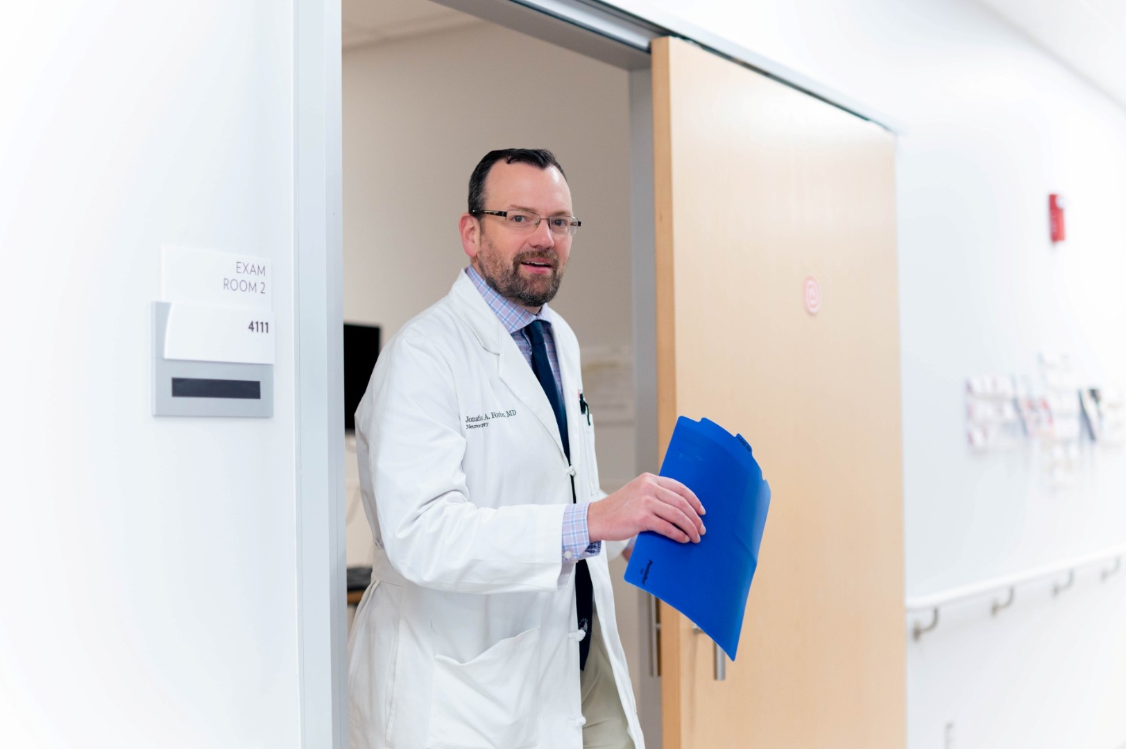 Physician walks from a medical room into the hallway. 