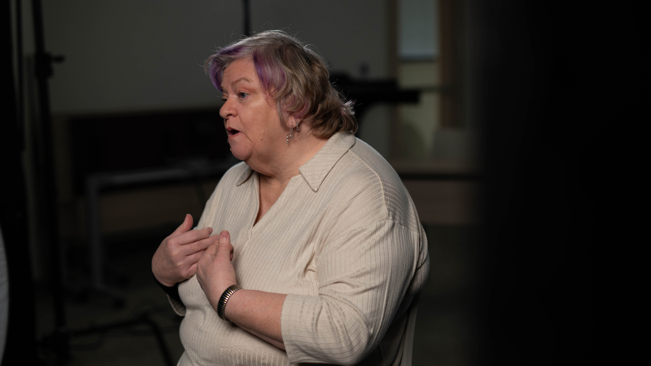 Connie gestures toward her chest while speaking with the interviewer