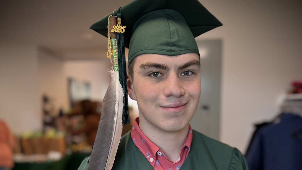 Deklan celebrates his high school graduation, proudly wearing his cap and gown adorned with a Native feather.
