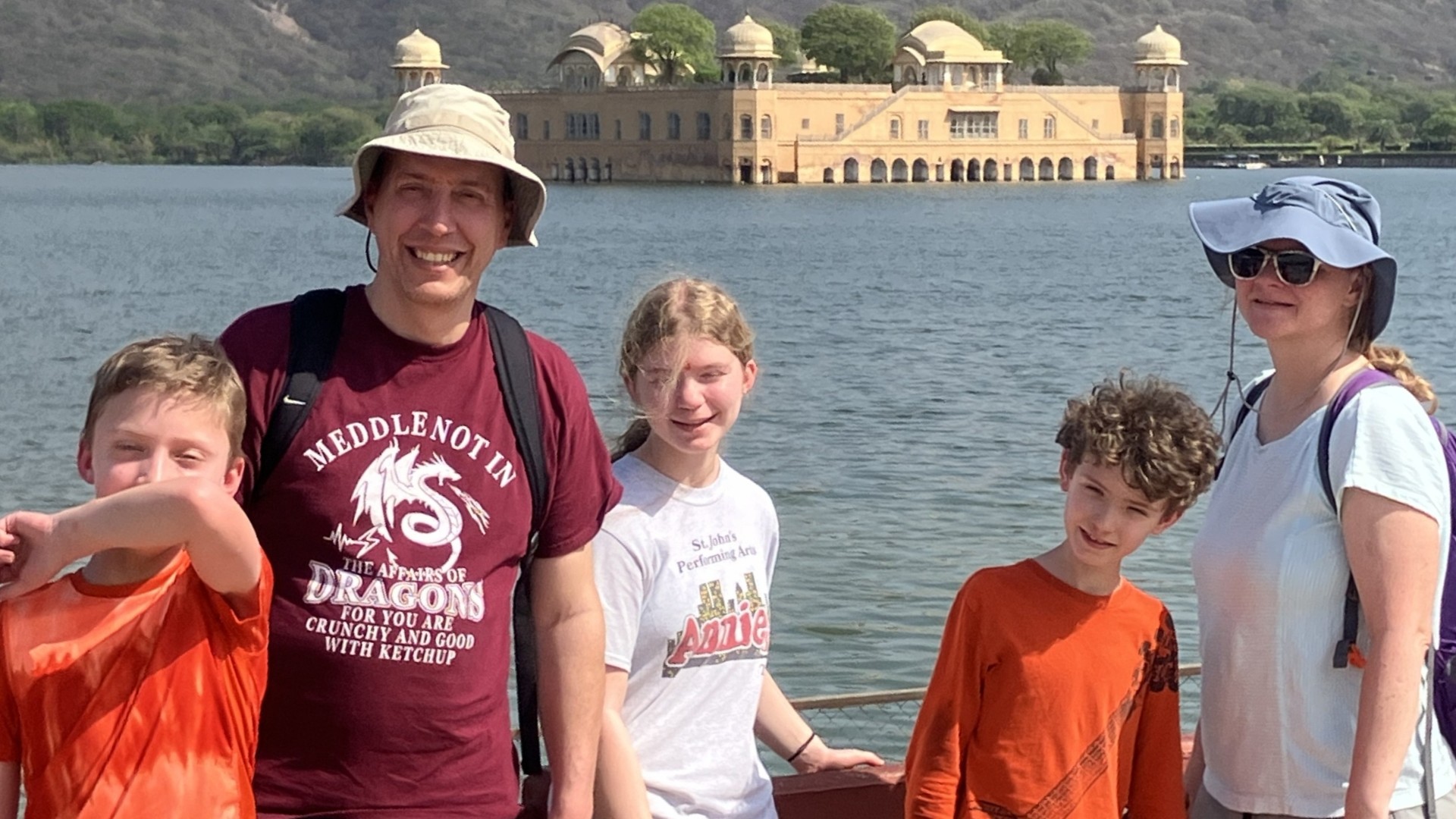 Mark and family stand on a platform next to a body of water with an ornamental building in the background. . 