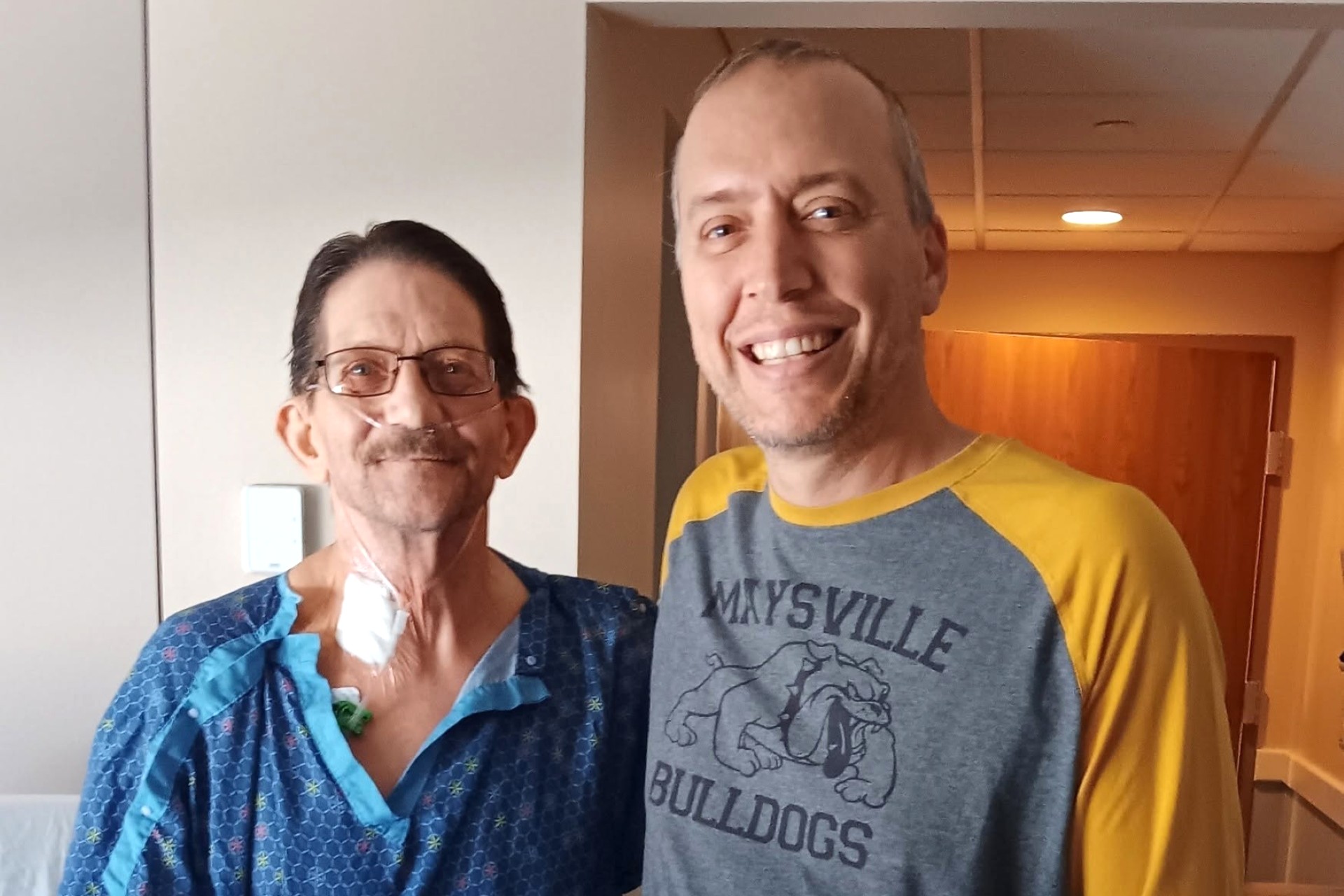 A patient recipient stands next to Mark in a medical setting. 