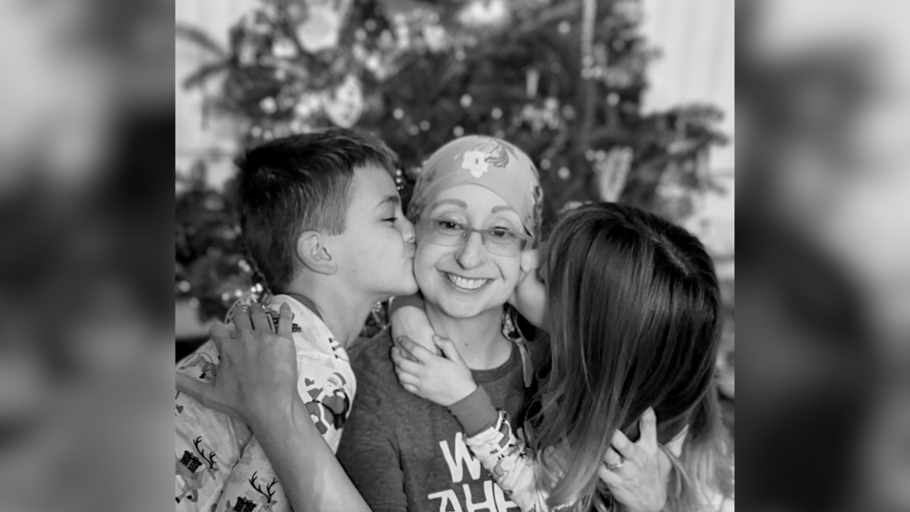 Mary gets kisses on the cheek from her children in front of the Christmas tree