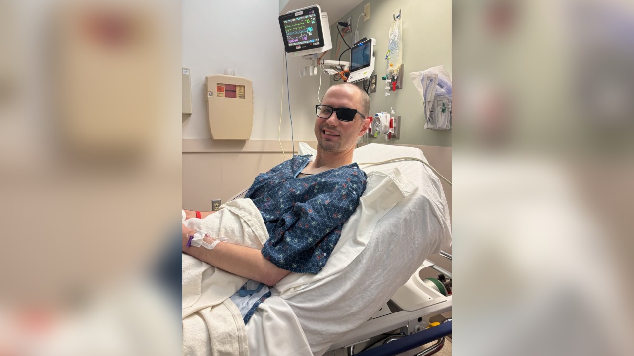 Patrick lies in a hospital bed and smiles for the camera.