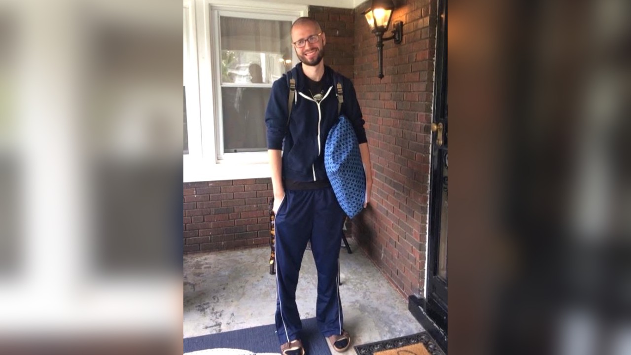 Patrick stands on a porch with a pillow in his hand.