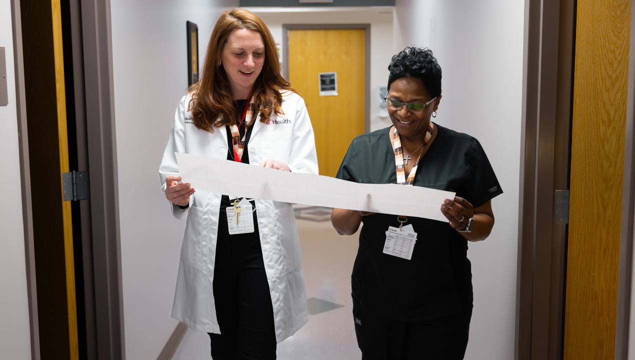 Two UC Health's Women's Pregnancy and Childbirth care team members walk down a hallway while looking at a print out together