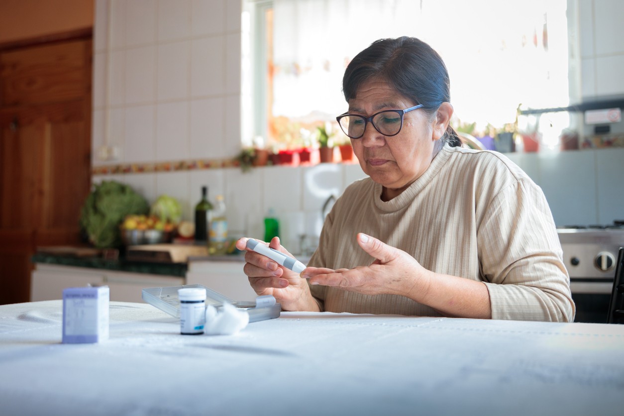 Woman uses a gluclose monitor at her kitchen table