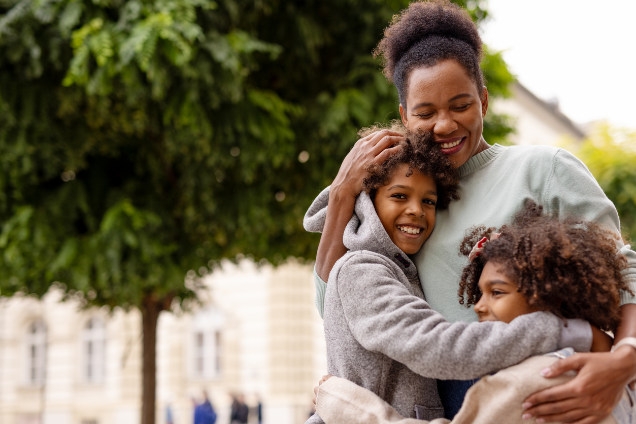 woman closely hugs two young children