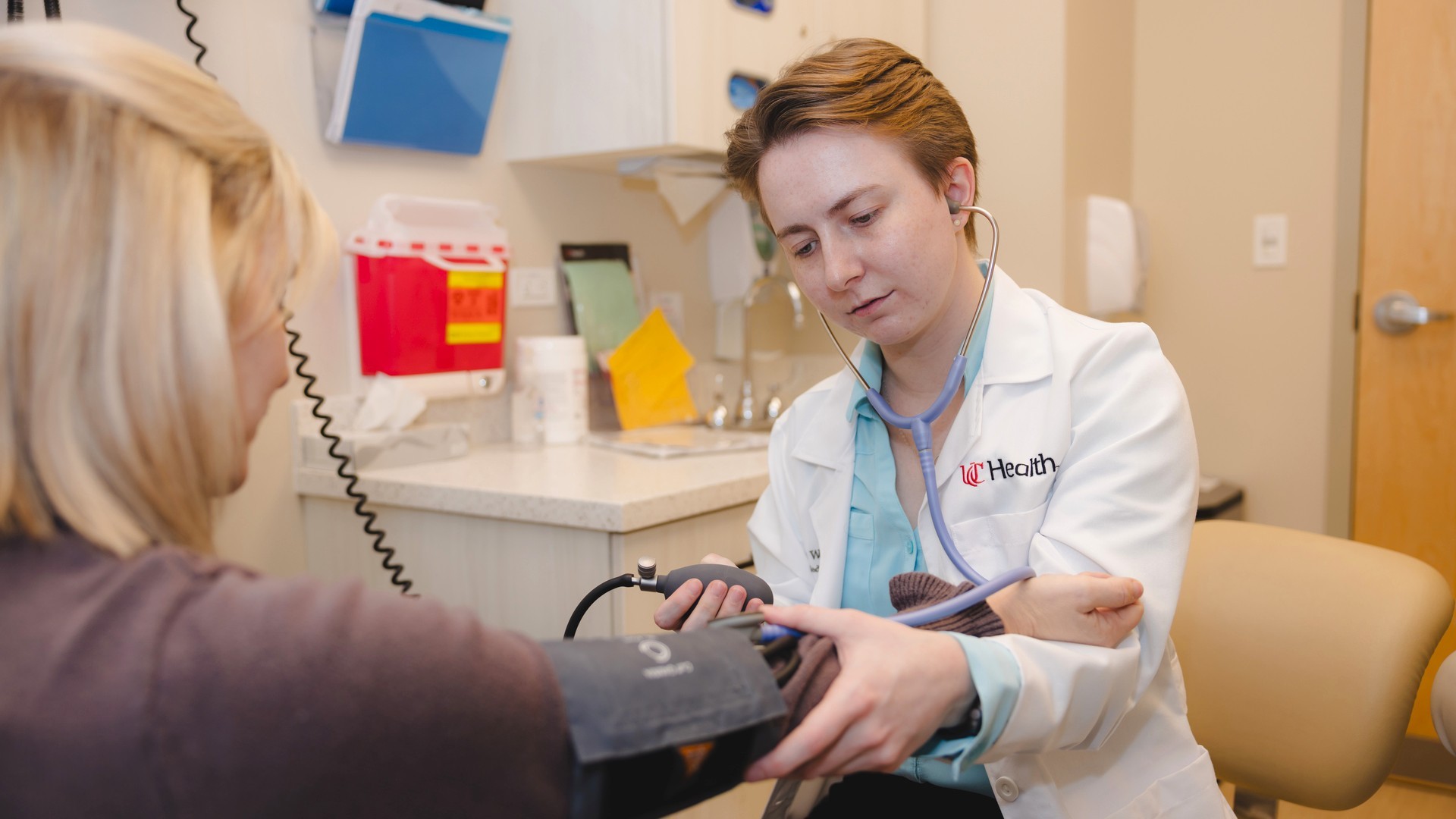A primary care provider measures the blood pressure of a patient in a medical setting. 