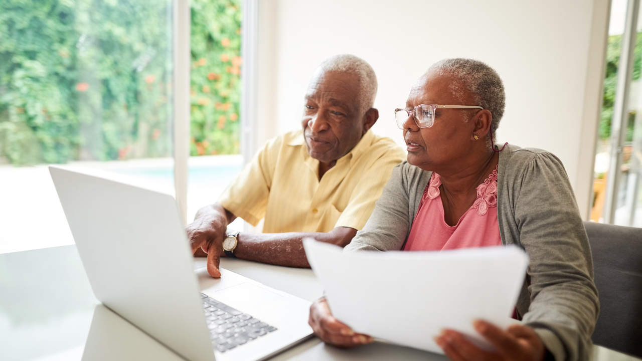 two older adults share laptop at kitchen table