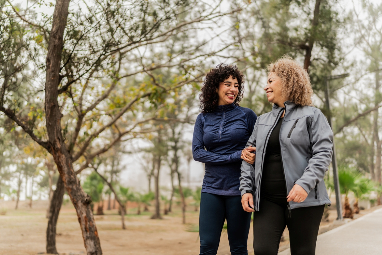 Two women walk outside in a park environment.