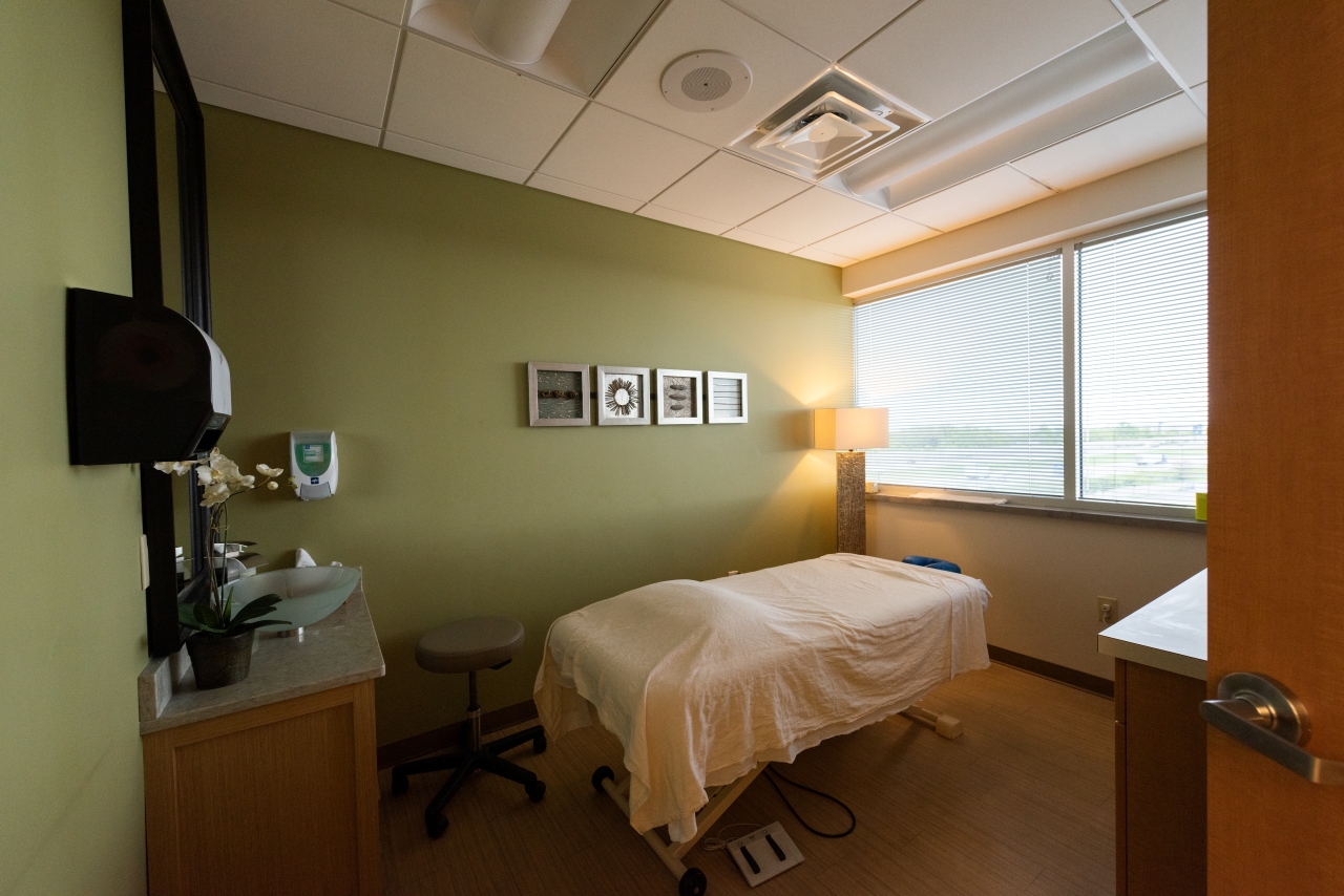 Image of massage therapy room with a bed and photos on a wall. 