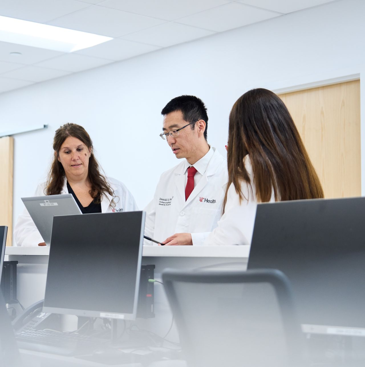 Three physicians talk next to computers.