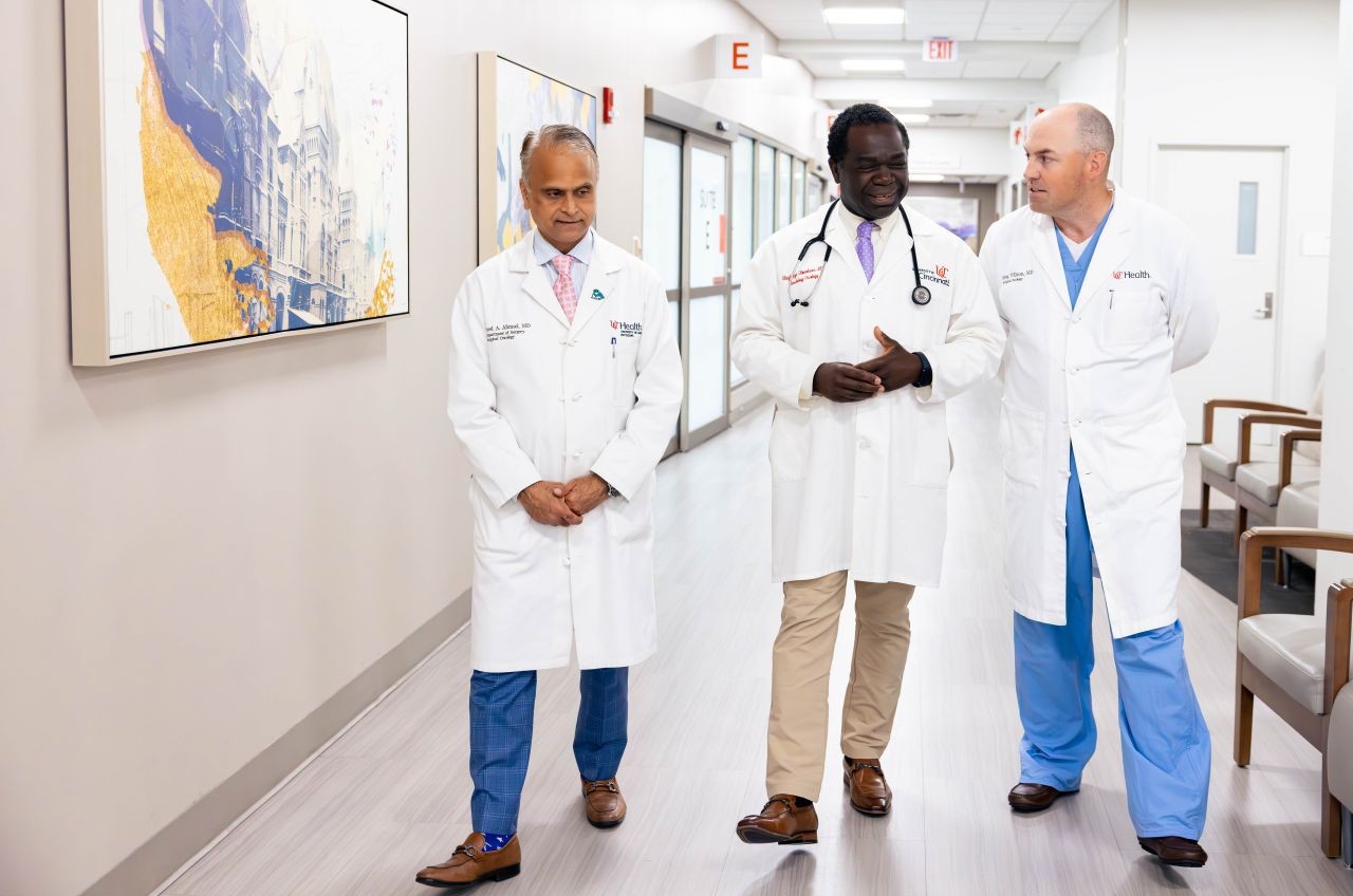 Three physicians talk as they walk through a hallway. 