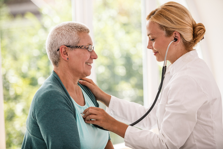 A doctor listening to a patient's lungs in the sunny clinic.