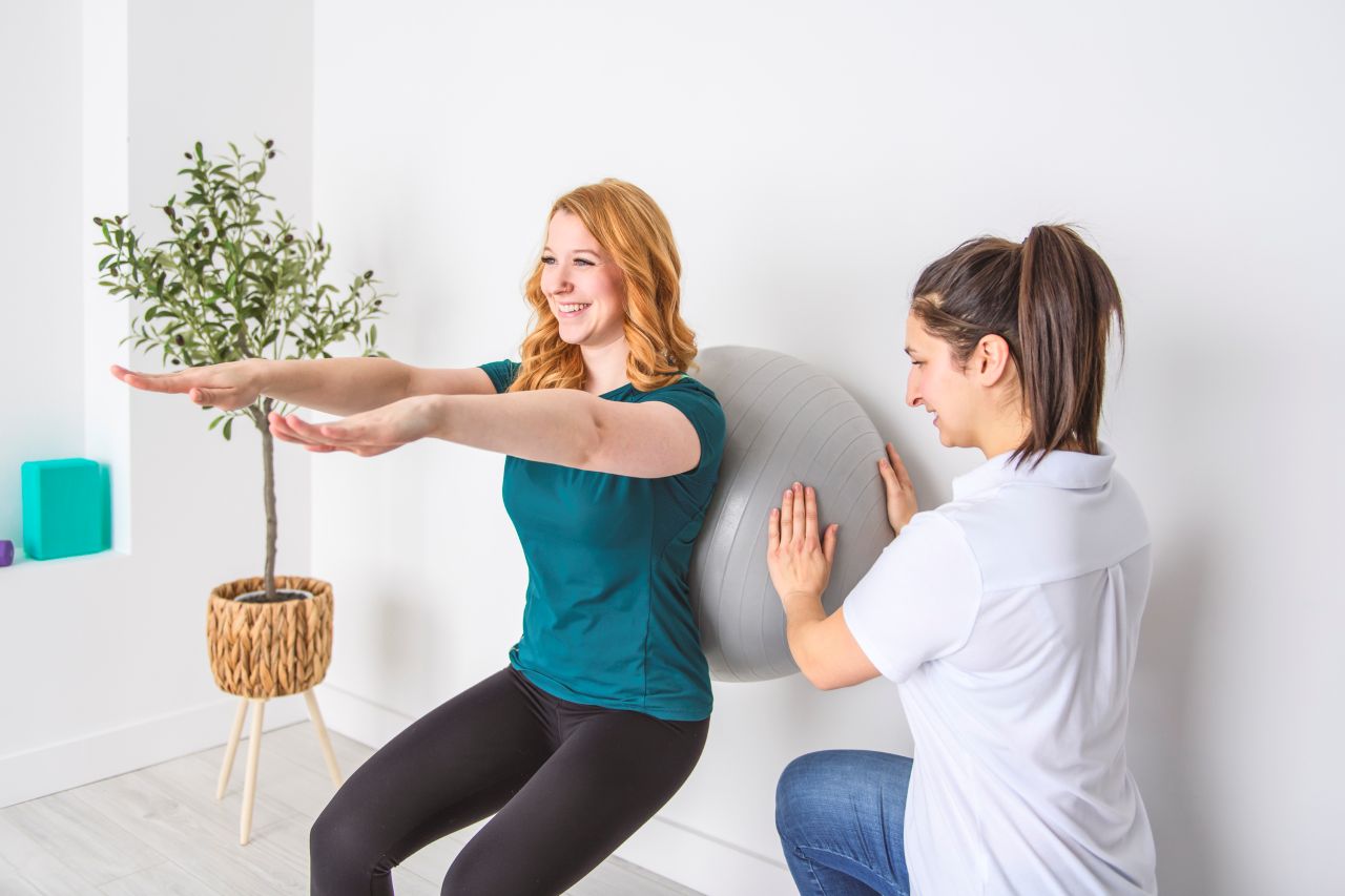 Woman exercises during a therapy session while a therapist assists to her side.