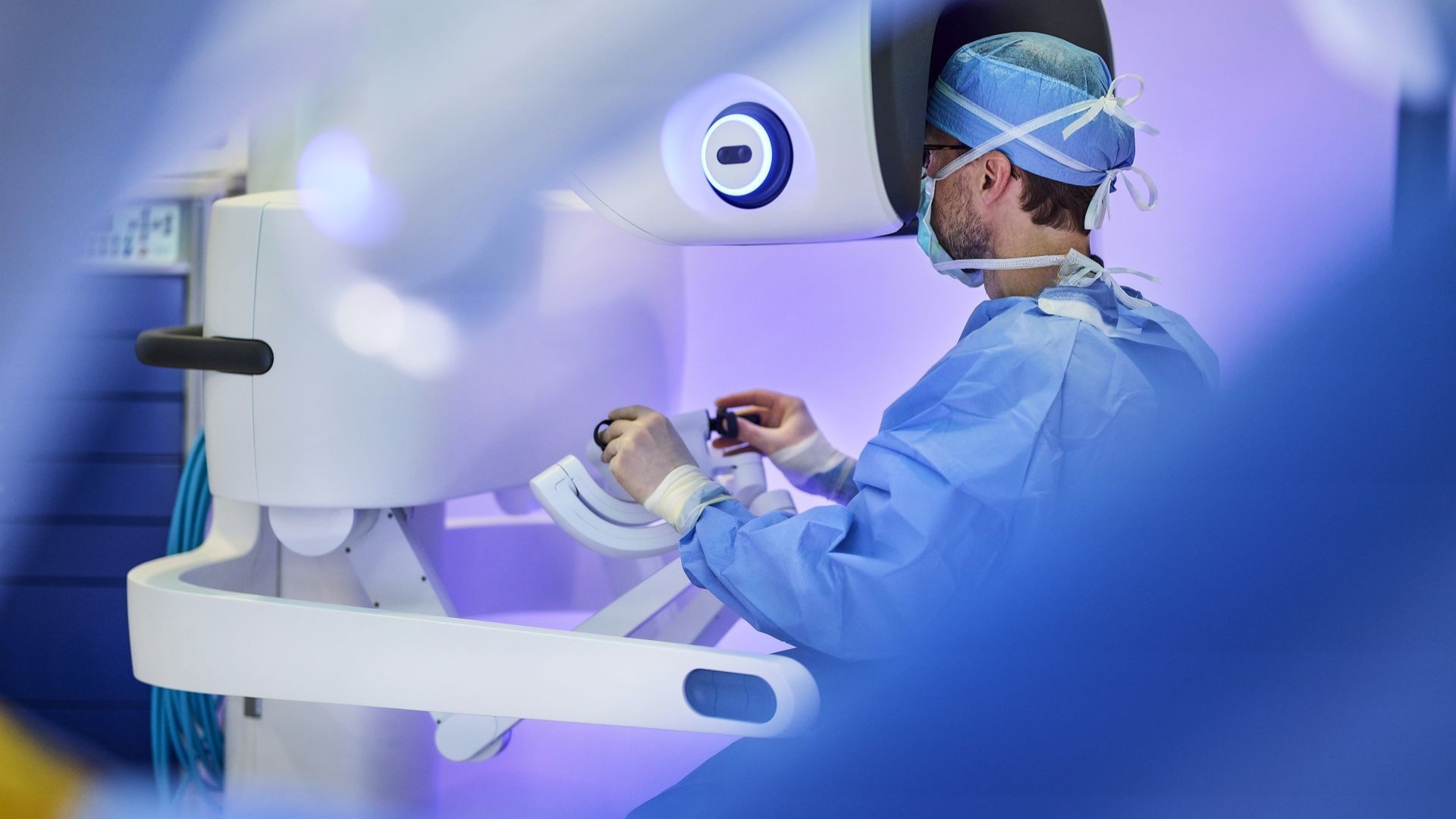 Physician in masks and scrubs works with a robotic device to perform a medical procedure.