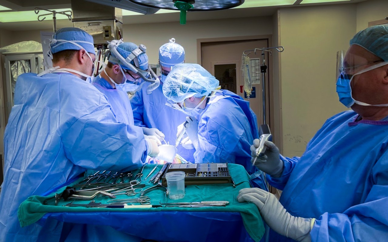 Physicians in masks and scrubs perform a medical procedure. 