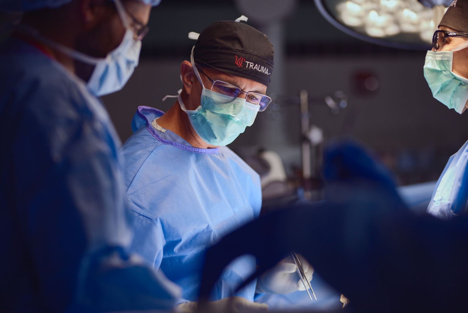 Physicians in masks and scrubs perform a medical procedure. 