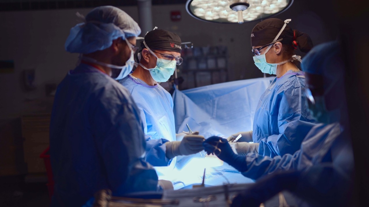 Physician in scrubs and masks perform surgery. 