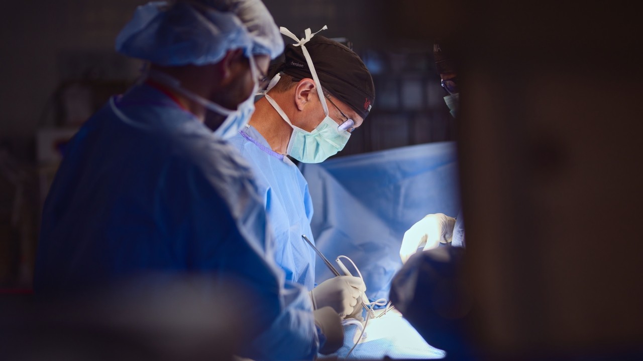 Physician in scrubs and masks perform surgery. 