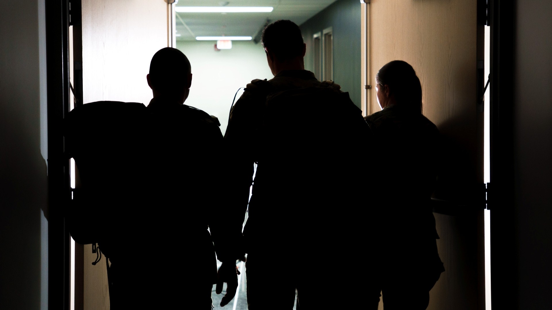 Three people walk through a set of doors. 