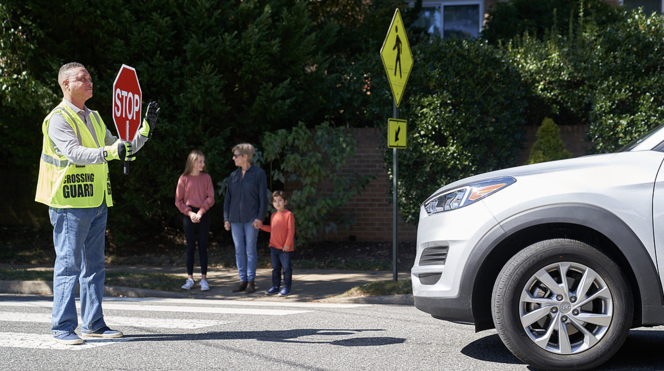 A family being directed to cross a cross-walk by a crossing gaurd.