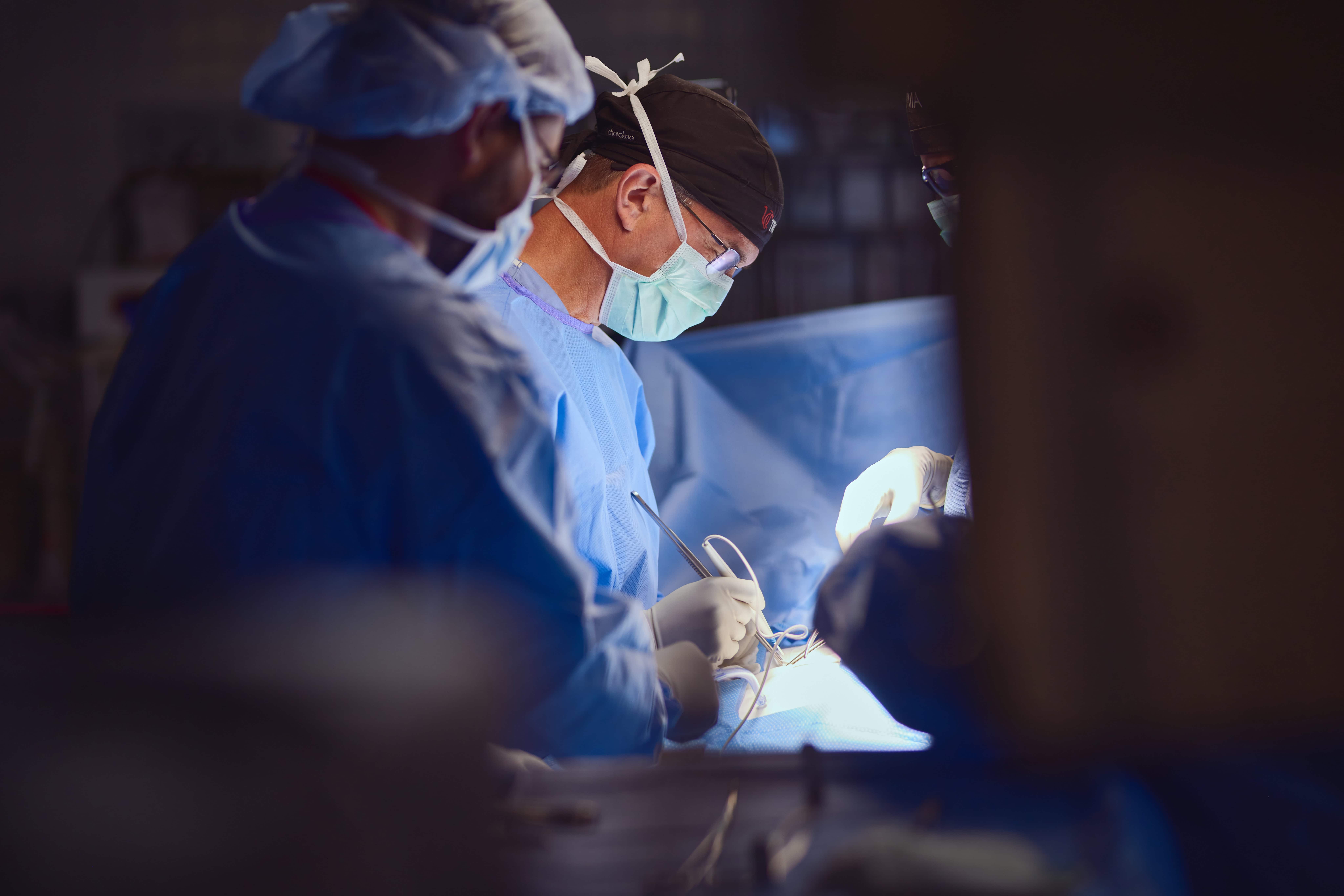 Physician in scrubs and masks perform surgery. 
